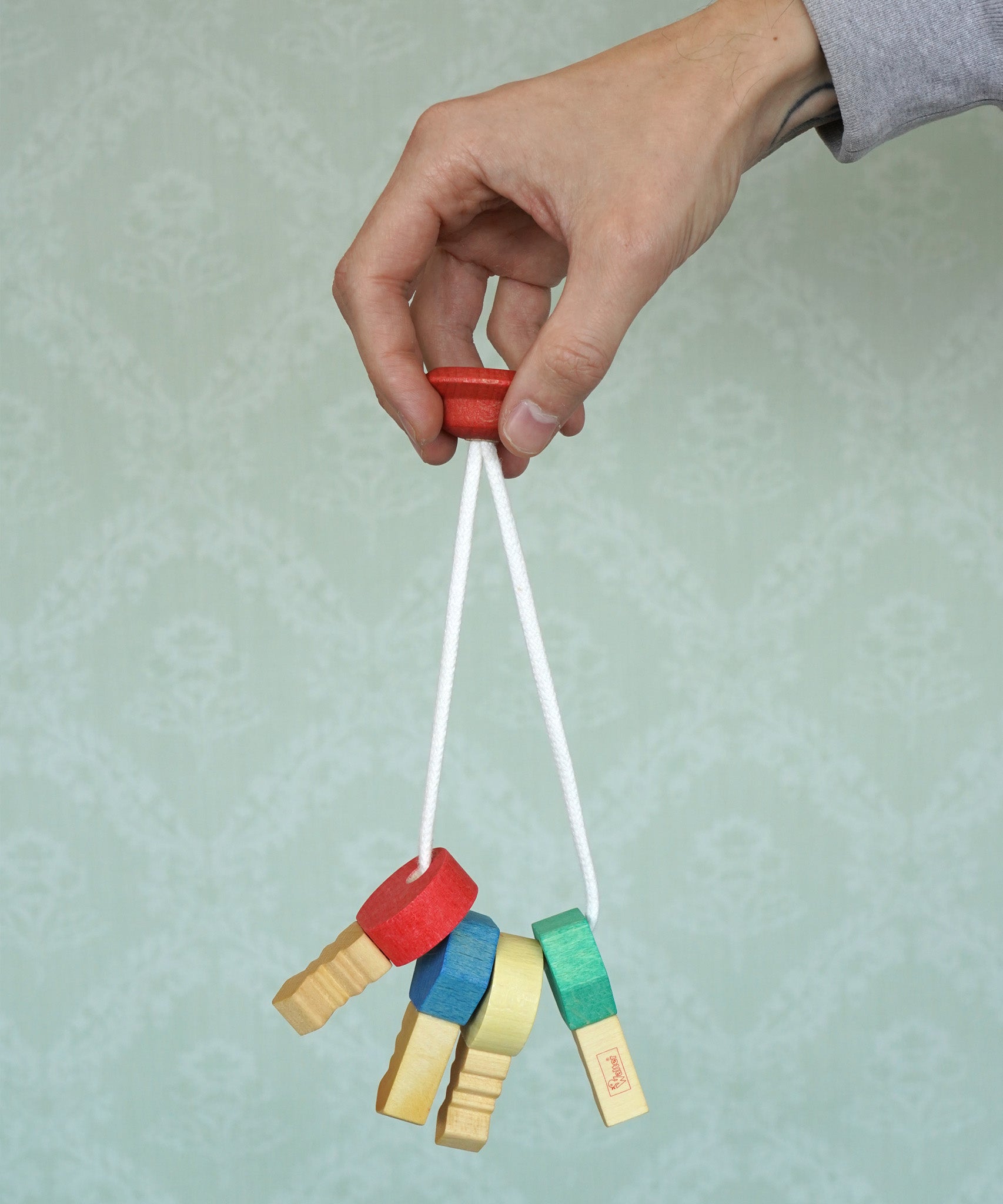 A adult hand holding the Nic Toys wooden grasping keyring set available at Babipur against a green decorative background.