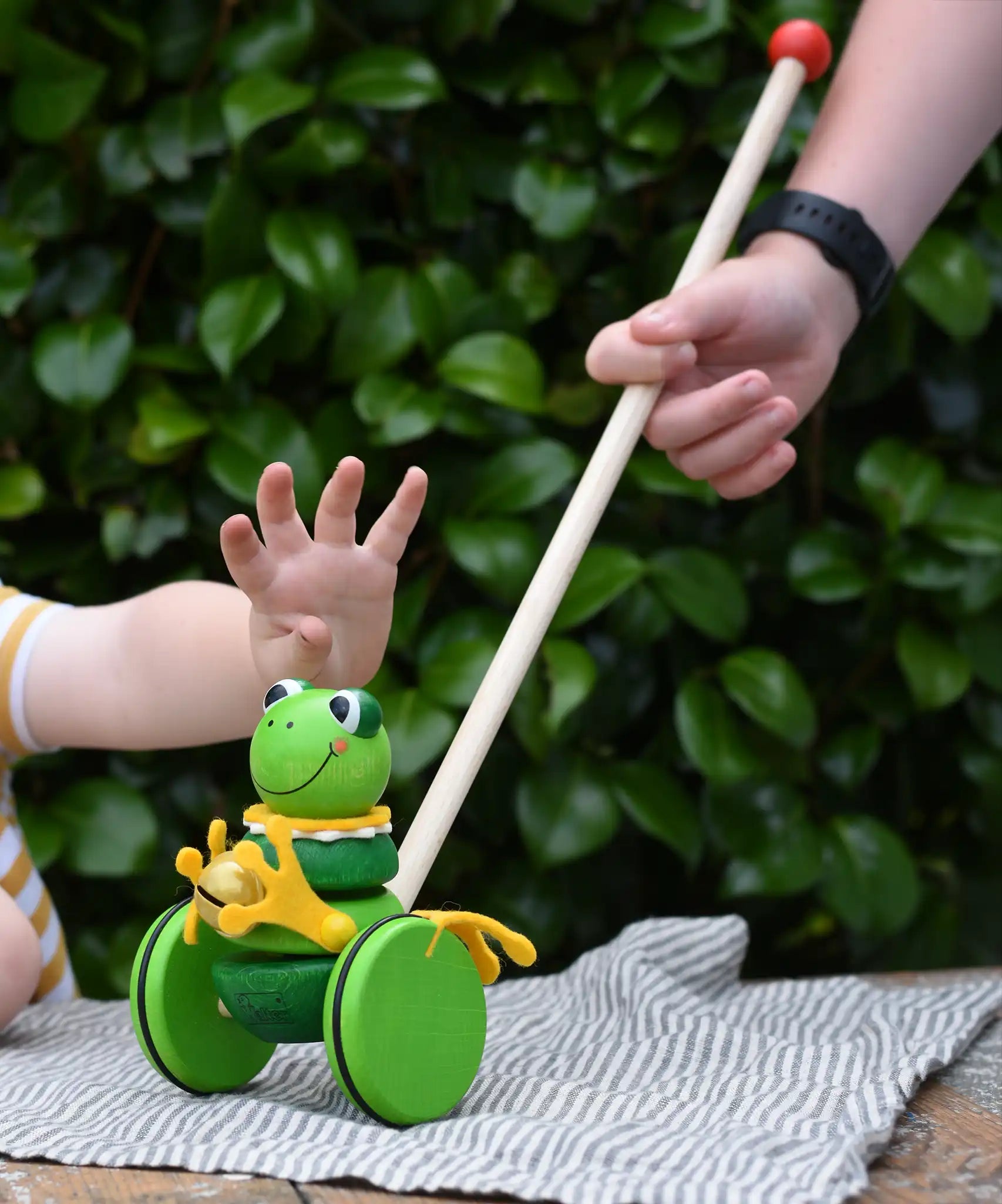 Children playing with the Nic Toys frog king push along toy. Green frog with yellow felt details and gold bell. 