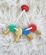 A close up of the Nic Toys wooden grasping keyring set available at Babipur on a white decorative blanket showing the different shaped keys.