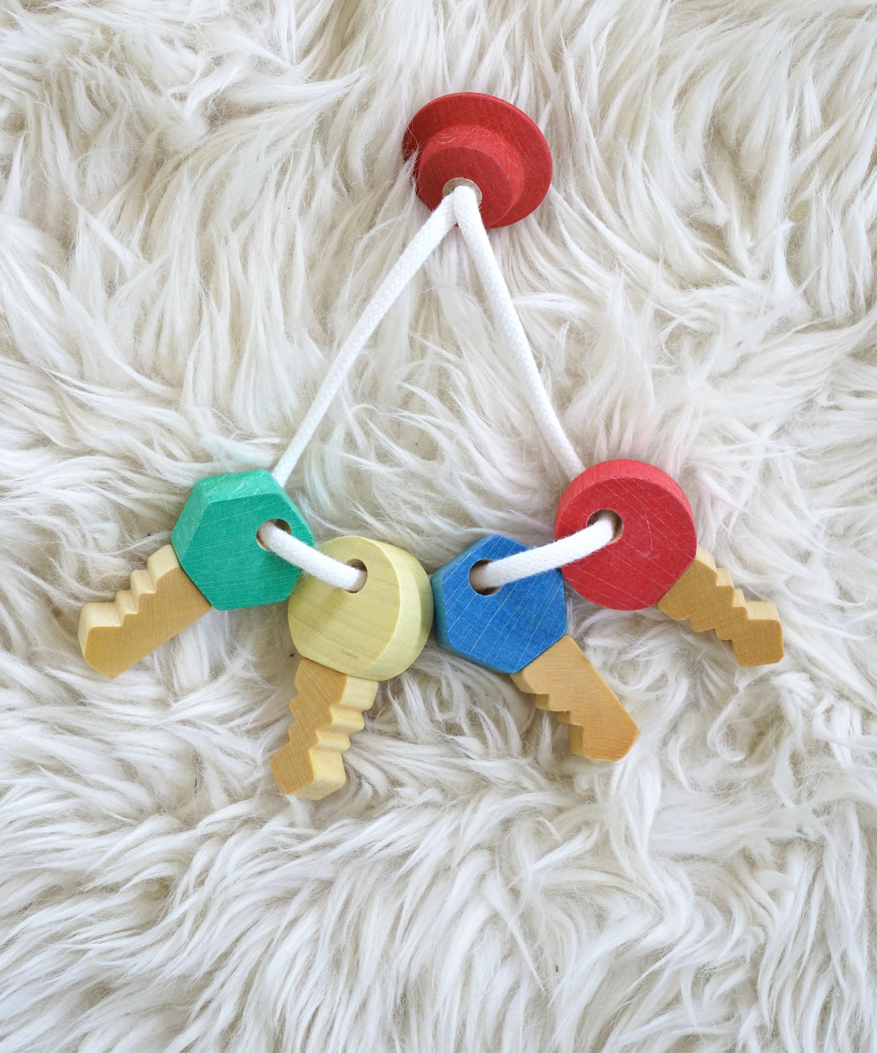 A close up of the Nic Toys wooden grasping keyring set available at Babipur on a white decorative blanket showing the different shaped keys.