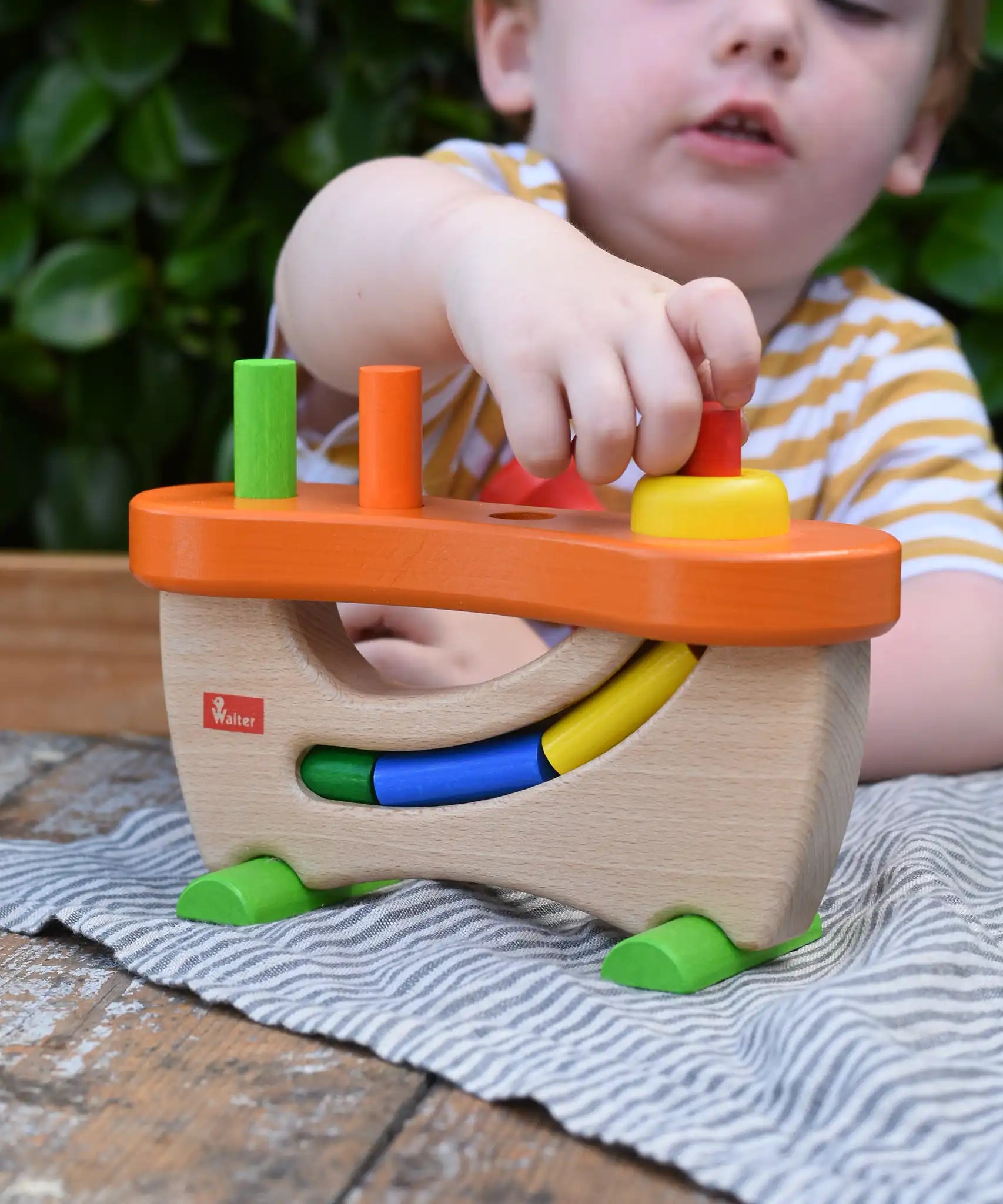 Child placing a cylinder block piece into the slot on the Nic wooden pounding bench hammering toy. 