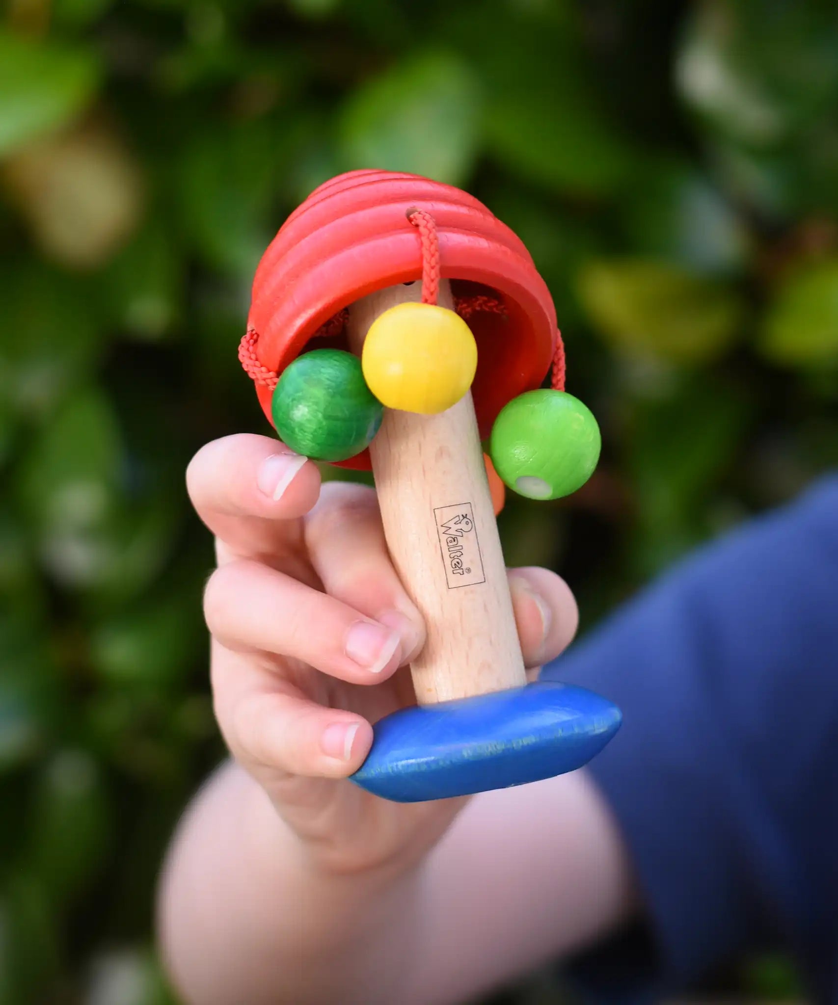 Nic mushroom wooden rattle toy in a child's hand.