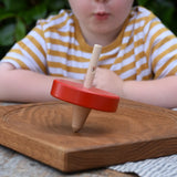 Nic Toys wooden red spinning top placed on a Mader oak spinning board. Features a wooden handle for handling the spinner top with a blue cord for spinning the top. 