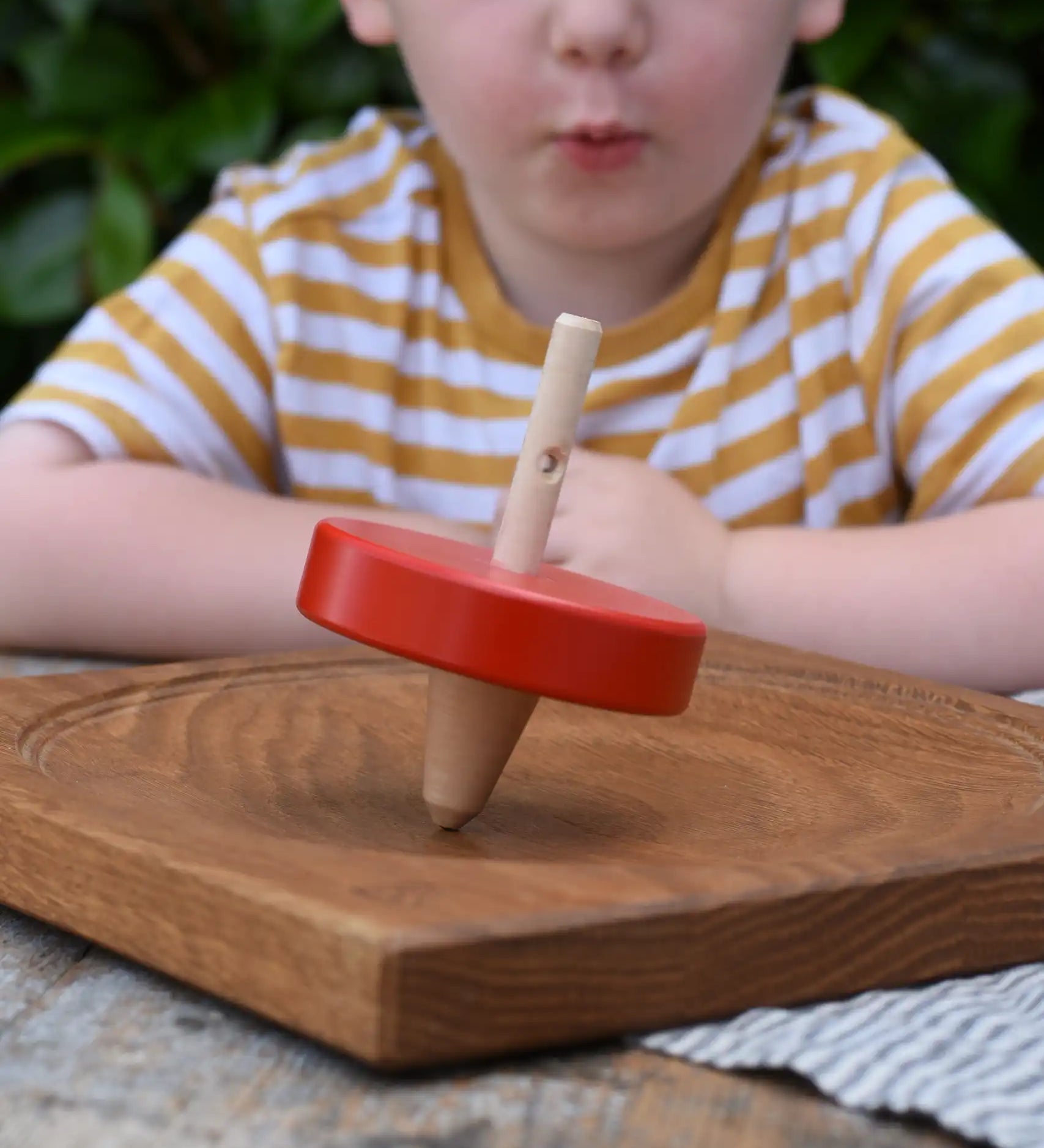 Nic Toys wooden red spinning top placed on a Mader oak spinning board. Features a wooden handle for handling the spinner top with a blue cord for spinning the top. 