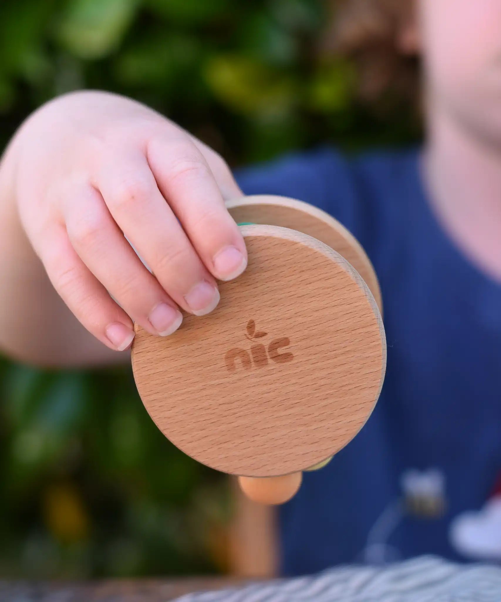 Nic Toys wooden rolling rattle in a child's hand. Roll along rattle with multicoloured beads.