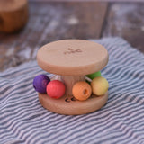 Nic Toys wooden rolling rattle placed on a wooden surface. Roll along rattle with multicoloured beads.