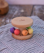 Nic Toys wooden rolling rattle placed on a wooden surface. Roll along rattle with multicoloured beads.