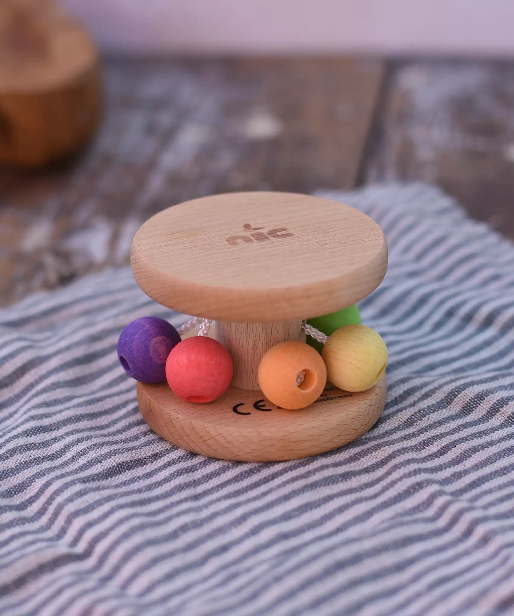 Nic Toys wooden rolling rattle placed on a wooden surface. Roll along rattle with multicoloured beads.