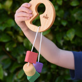 Child holding up the Nic Toys wooden threaded shape sorter. Wooden disk with a keyhole shape cut out in the middle with a piece of thread feeding through different coloured blocks in different coloured shapes.