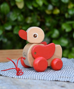 Nic waggle duck pull along wooden toy placed on a grey striped cloth.