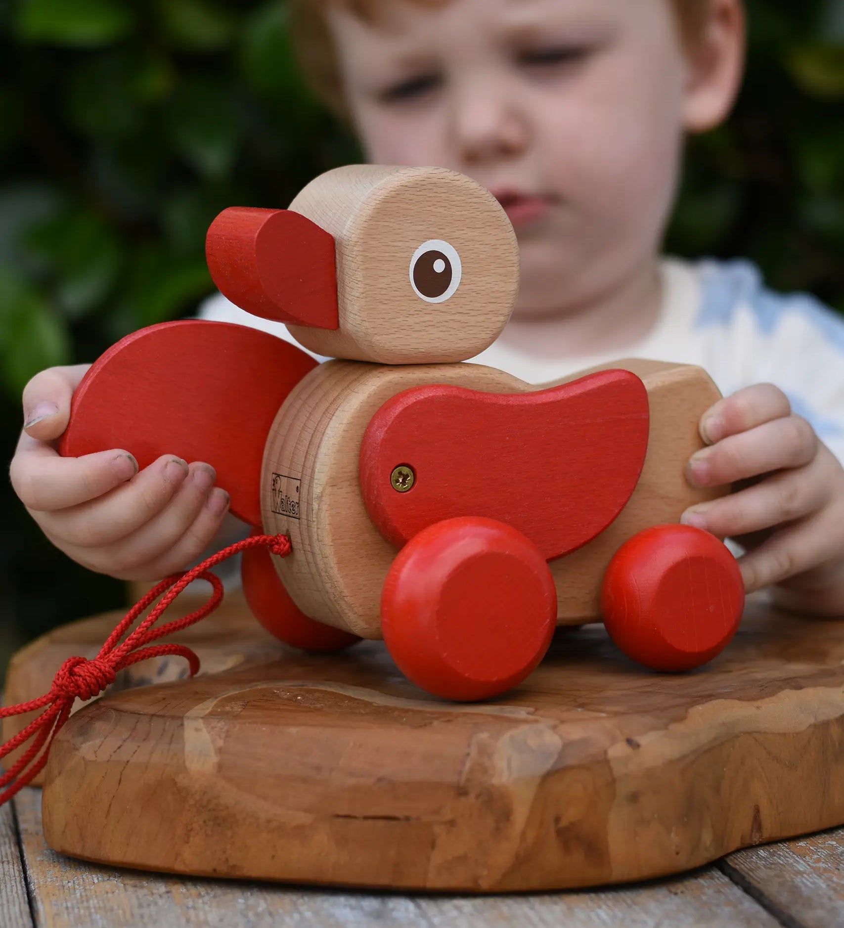 Child playing with the Nic waggle duck pull along wooden toy, moving it's red wings around.