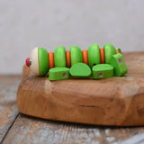 Side of the Nic Willy the centipede green wooden baby toy placed on a wooden surface.