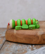 Side of the Nic Willy the centipede green wooden baby toy placed on a wooden surface.