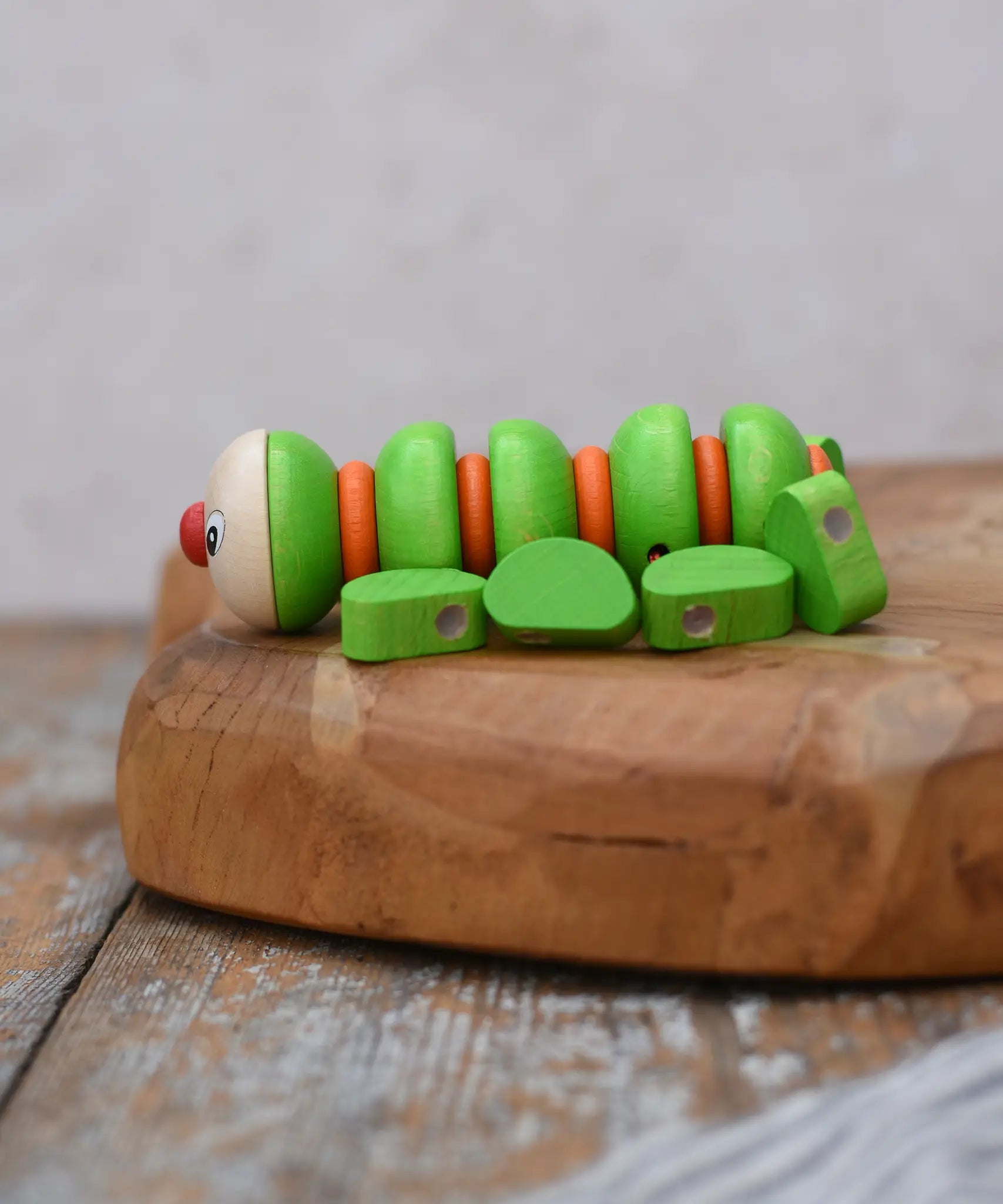 Side of the Nic Willy the centipede green wooden baby toy placed on a wooden surface.