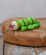 Nic Willy the centipede green wooden baby toy placed on a wooden surface. 