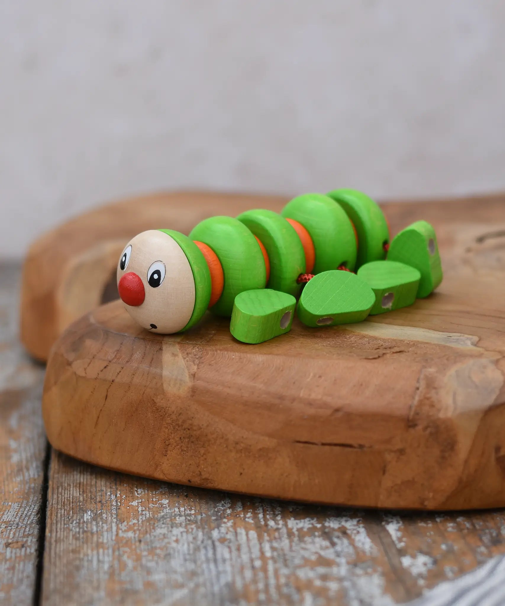 Nic Willy the centipede green wooden baby toy placed on a wooden surface. 