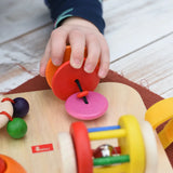 Close up of a child's hand pulling the rattling tree top attached to the Nic Wooden Baby Game busy Board with 4 four activities.