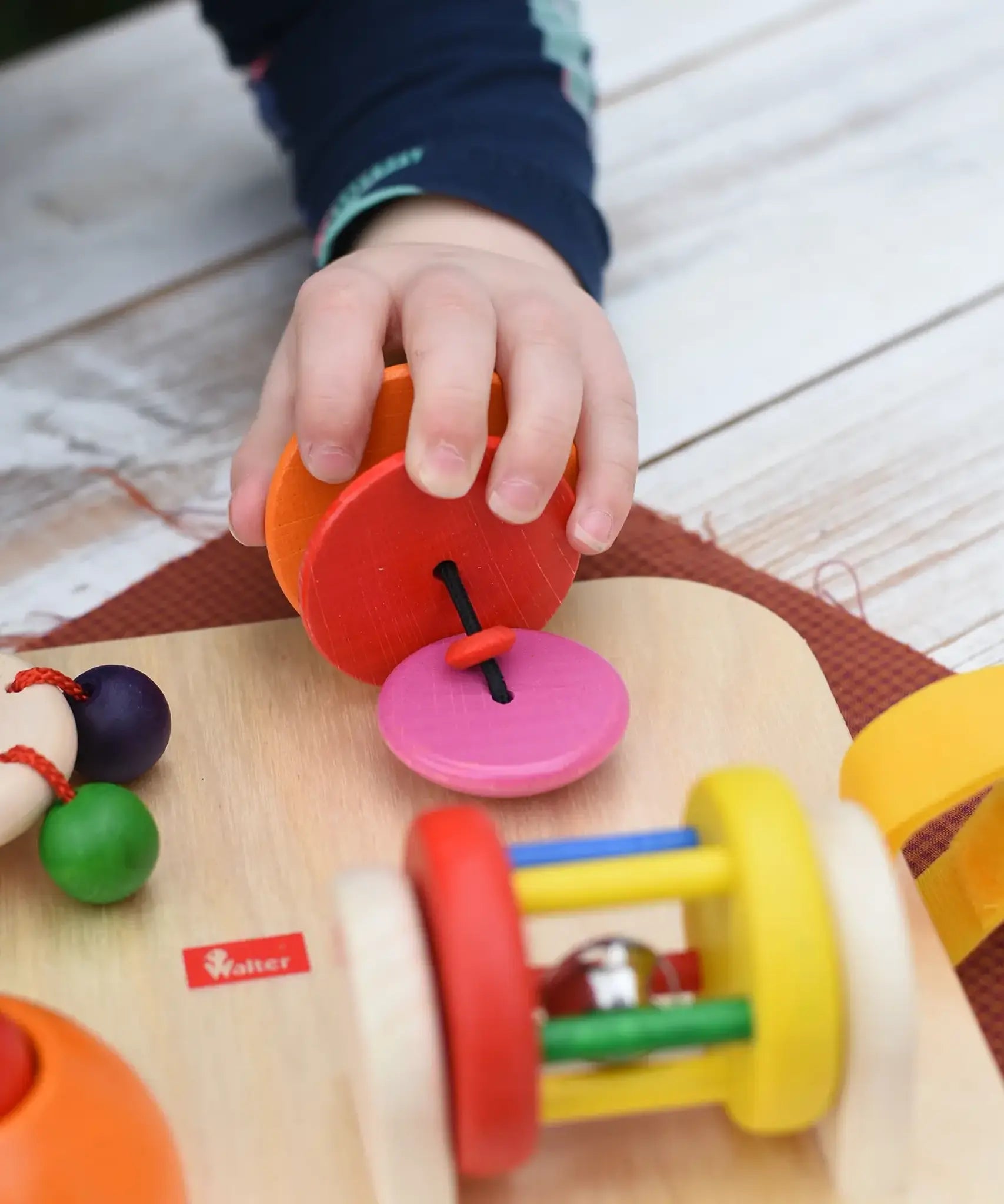 Close up of a child's hand pulling the rattling tree top attached to the Nic Wooden Baby Game busy Board with 4 four activities.