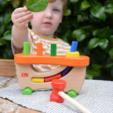 Child standing behind the Nic wooden pounding bench hammering toy.