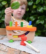 Child standing behind the Nic wooden pounding bench hammering toy.
