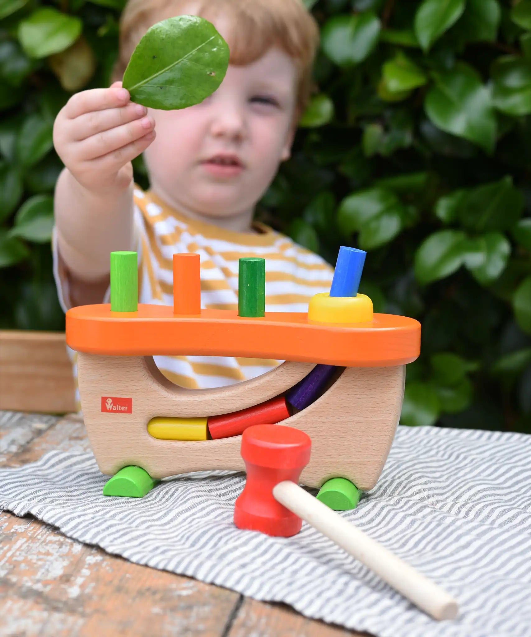 Child standing behind the Nic wooden pounding bench hammering toy.