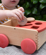 Child posting a Grapat coin into the long slot on the Nic wooden carriage shape sorter pull along toy.