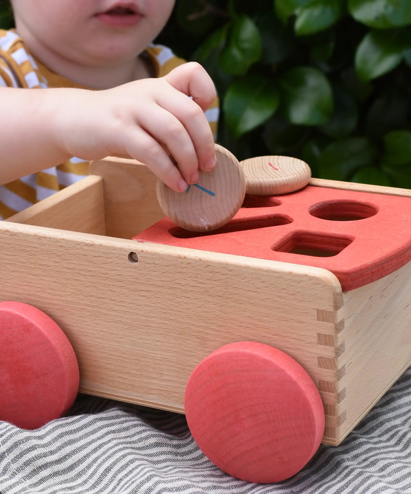 Child posting a Grapat coin into the long slot on the Nic wooden carriage shape sorter pull along toy.