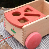 Close up of the shaped slots on the red lid of the Nic wooden carriage shape sorter pull along toy. 