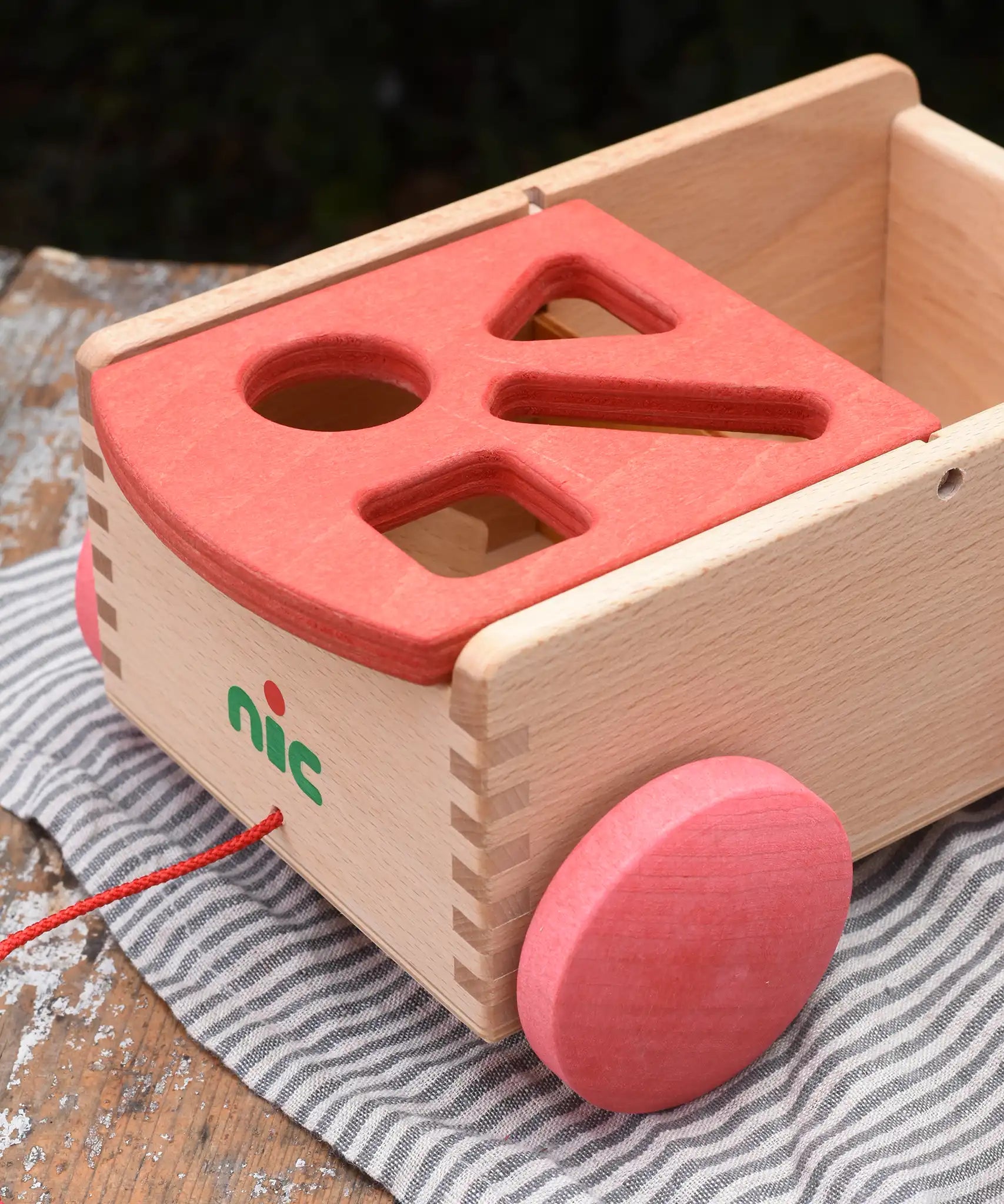 Close up of the shaped slots on the red lid of the Nic wooden carriage shape sorter pull along toy. 
