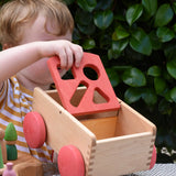 Child holding the Nic wooden carriage shape sorter pull along toy moving the red top. 8 wooden blocks in various shapes and colours.