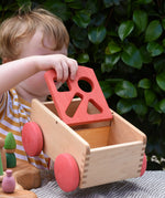 Child holding the Nic wooden carriage shape sorter pull along toy moving the red top. 8 wooden blocks in various shapes and colours.