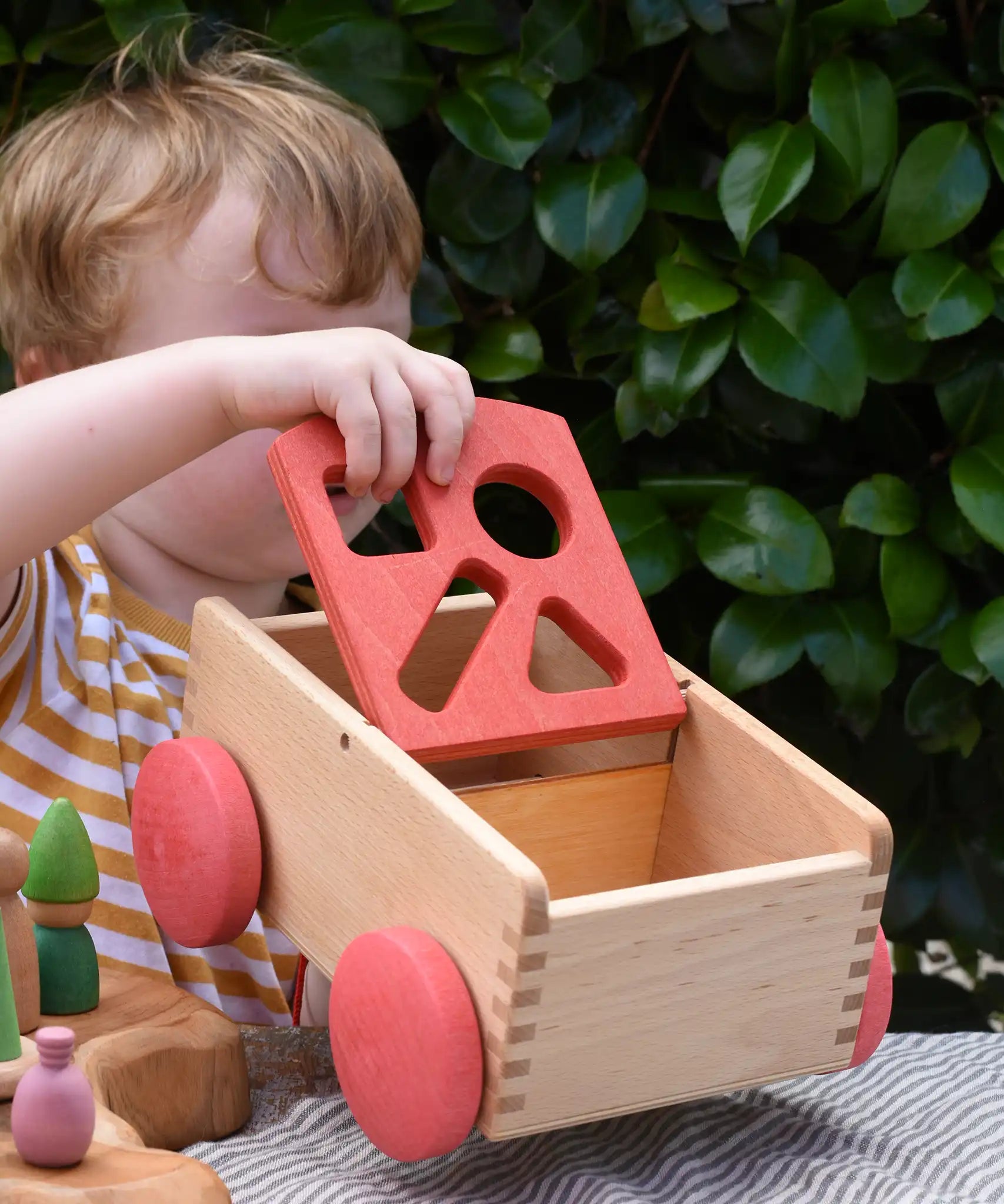 Child holding the Nic wooden carriage shape sorter pull along toy moving the red top. 8 wooden blocks in various shapes and colours.
