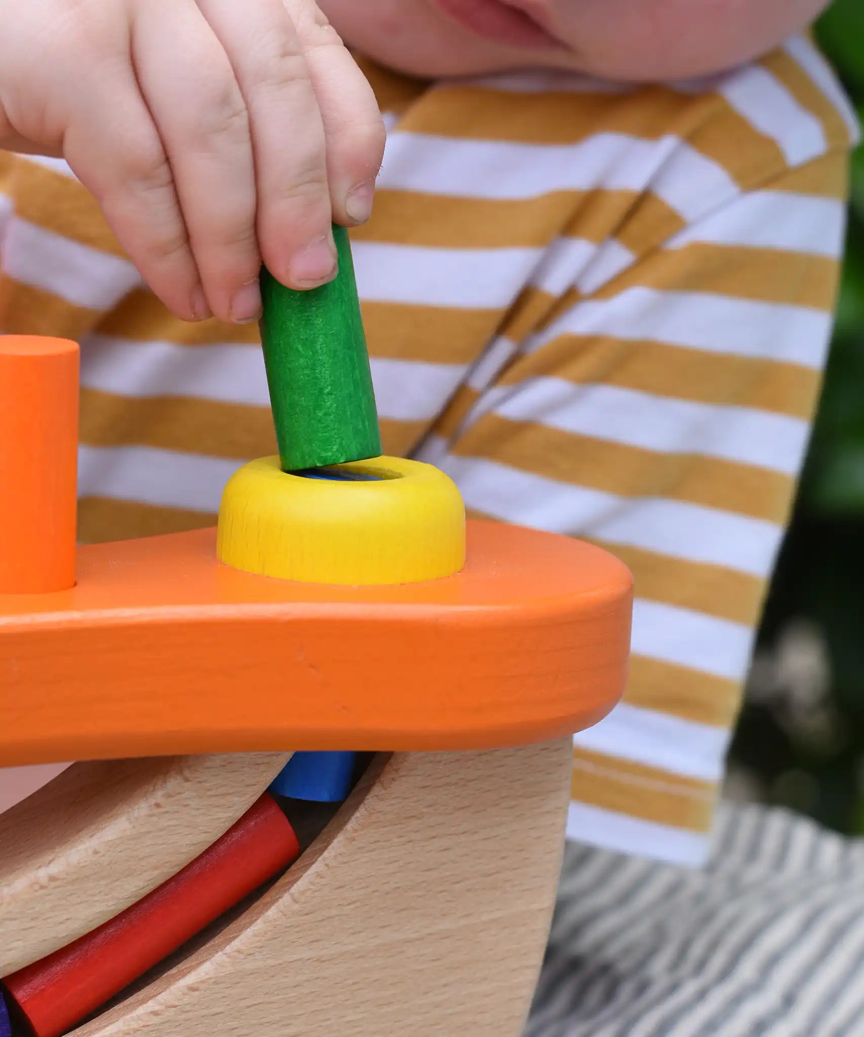 Close up of a child placing a cylinder shaped block into the slot in the Nic wooden pounding bench hammering toy.