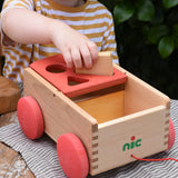 Child placing a rectangular shaped block into the slot on the Nic wooden carriage shape sorter pull along toy.