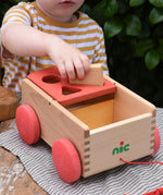 Child placing a rectangular shaped block into the slot on the Nic wooden carriage shape sorter pull along toy.