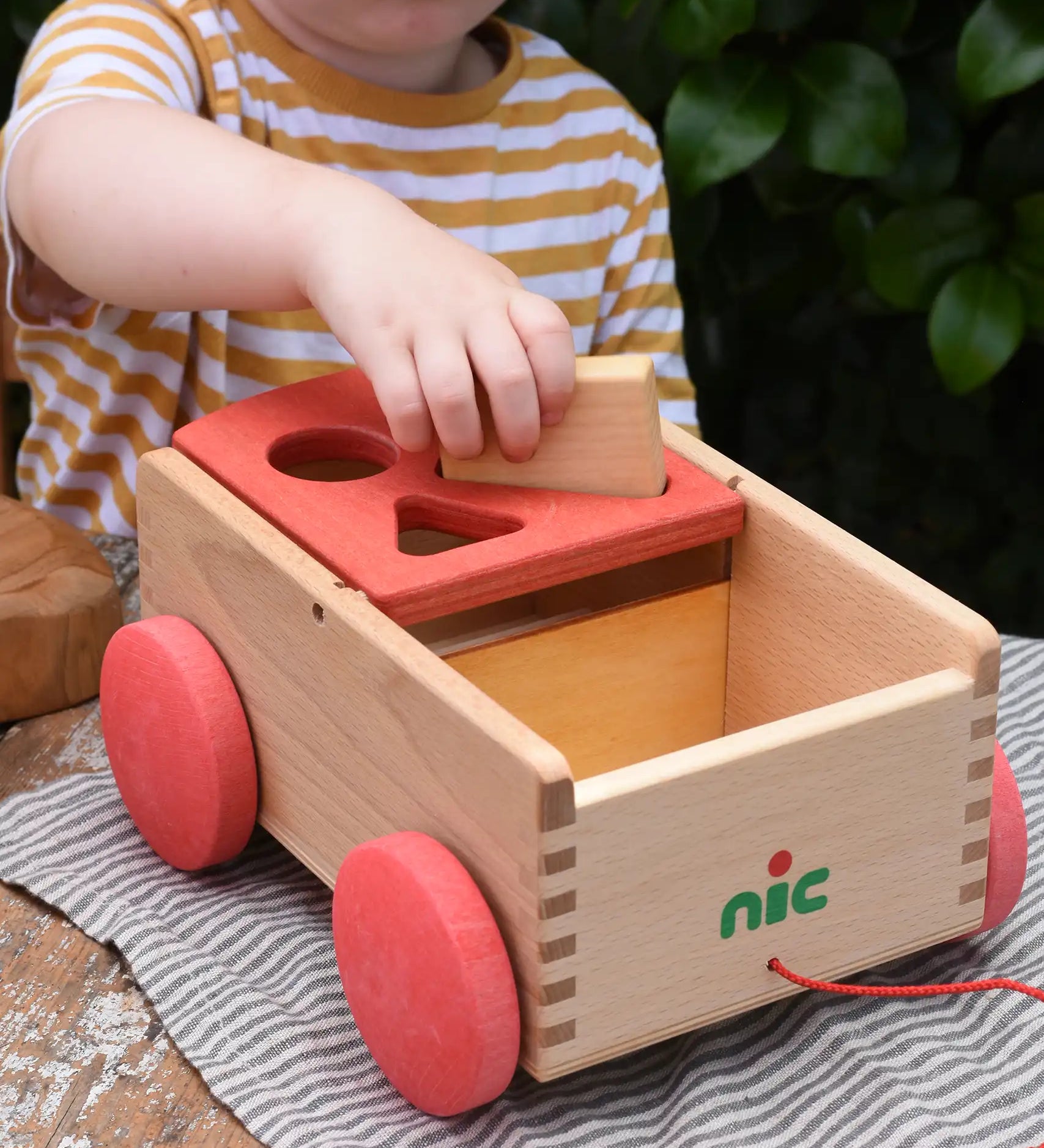 Child placing a rectangular shaped block into the slot on the Nic wooden carriage shape sorter pull along toy.