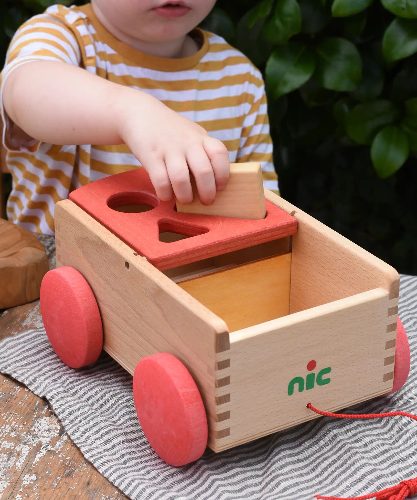 Child placing a rectangular shaped block into the slot on the Nic wooden carriage shape sorter pull along toy.