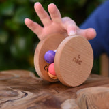 Child's hand pushing the Nic Toys wooden rolling rattle along a wooden surface. Roll along rattle with multicoloured beads.