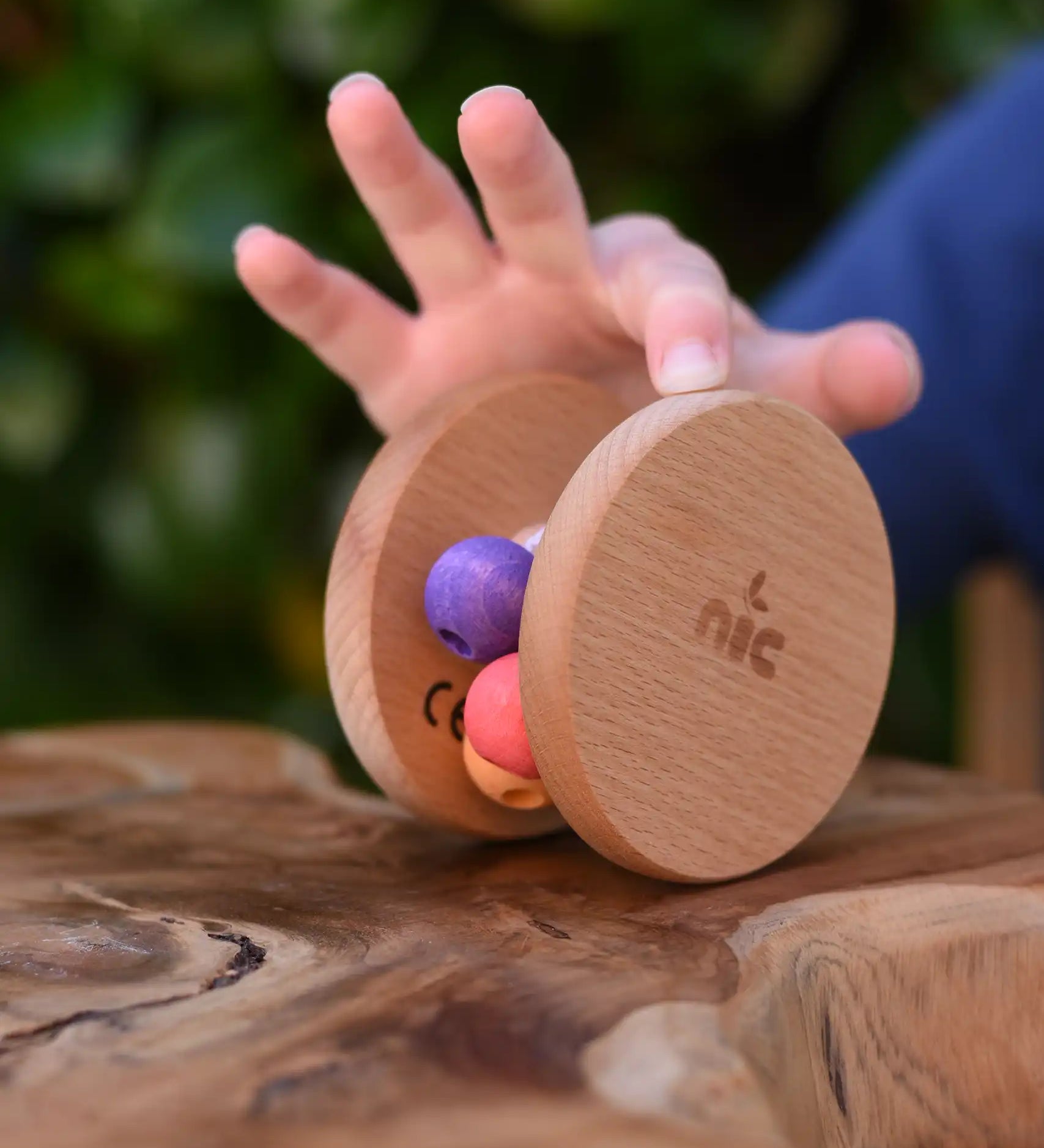 Child's hand pushing the Nic Toys wooden rolling rattle along a wooden surface. Roll along rattle with multicoloured beads.