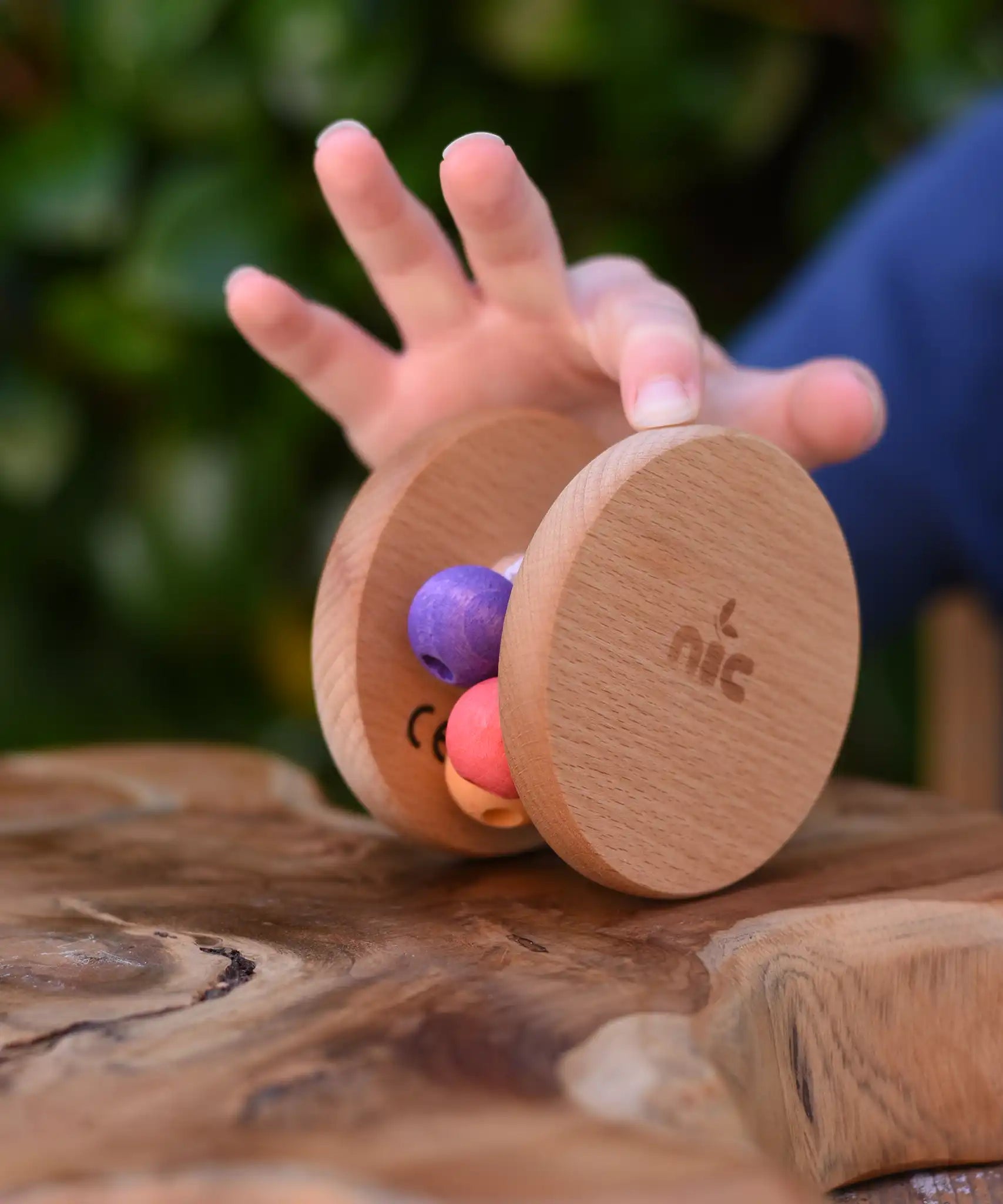 Child's hand pushing the Nic Toys wooden rolling rattle along a wooden surface. Roll along rattle with multicoloured beads.