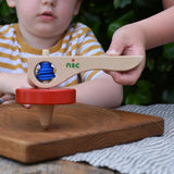 Nic Toys wooden red spinning top on an oak Mace spinning plate. Features a wooden handle for handling the spinner top with a blue cord for spinning the top. 