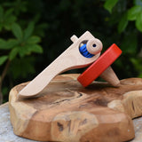 Nic Toys wooden red spinning top placed on a wooden surface outdoors. Features a wooden handle for handling the spinner top with a blue cord for spinning the top. 