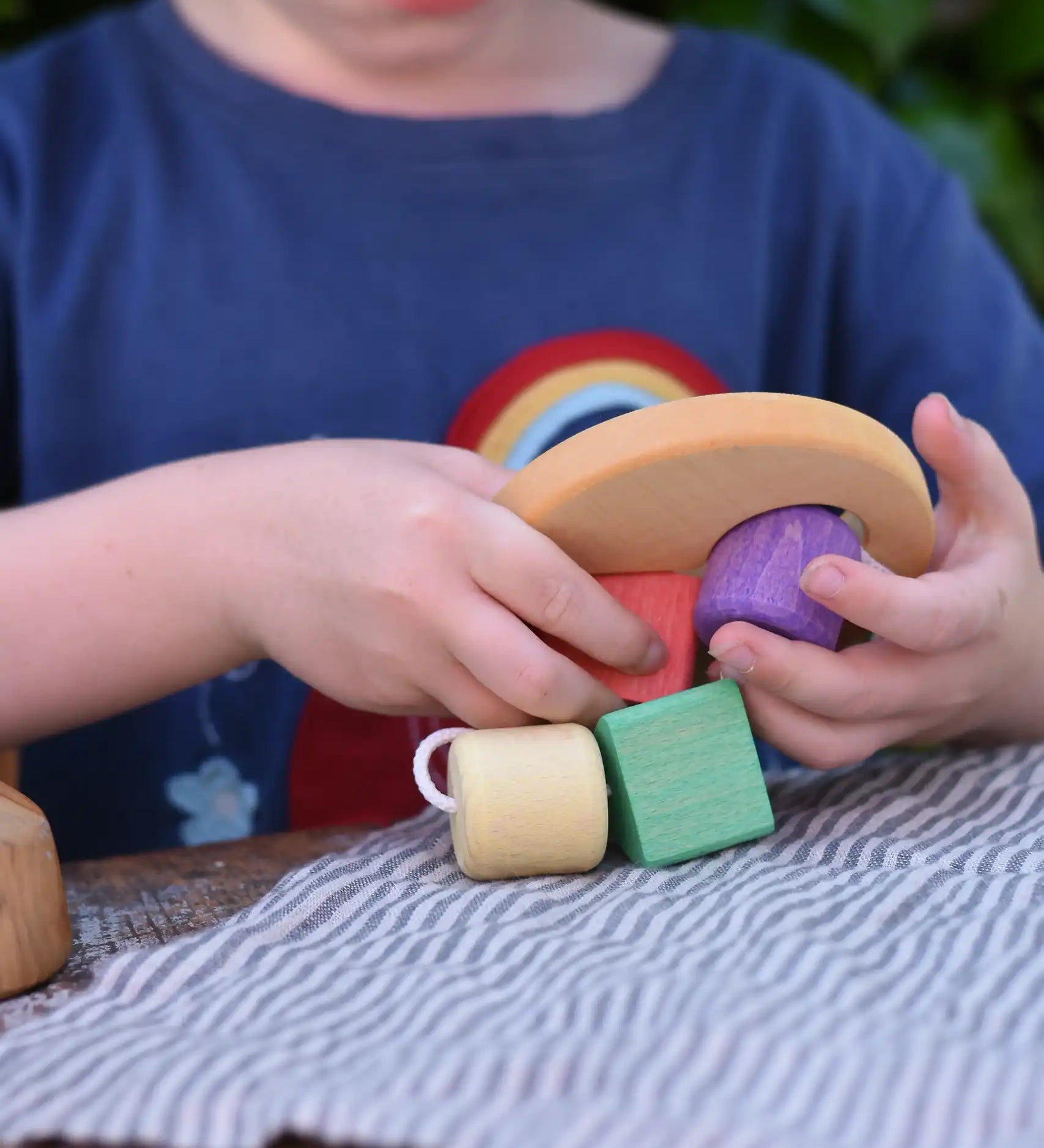 Child playing with the Nic Toys wooden threaded shape sorter. Wooden disk with a keyhole shape cut out in the middle with a piece of thread feeding through different coloured blocks in different coloured shapes.