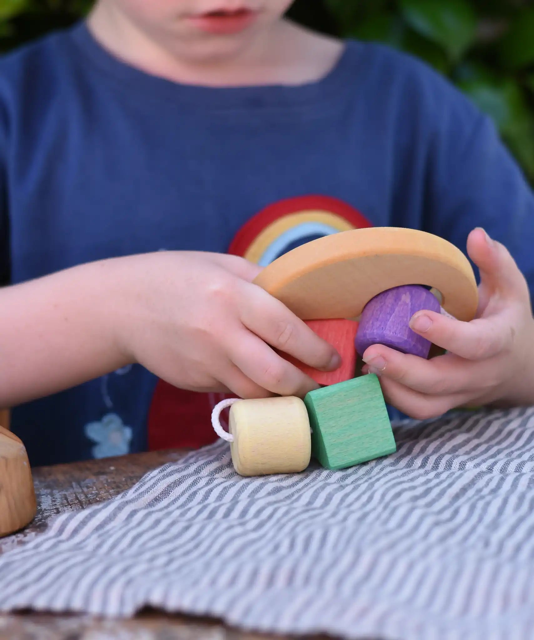 Child playing with the Nic Toys wooden threaded shape sorter. Wooden disk with a keyhole shape cut out in the middle with a piece of thread feeding through different coloured blocks in different coloured shapes.