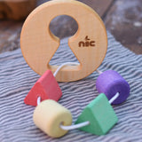 Nic Toys wooden threaded shape sorter placed on a cloth on a wooden surface. Wooden disk with a keyhole shape cut out in the middle with a piece of thread feeding through different coloured blocks in different coloured shapes.
