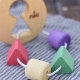 Close up of the coloured shape pieces on the Nic Toys wooden threaded shape sorter. Wooden disk with a keyhole shape cut out in the middle with a piece of thread feeding through different coloured blocks in different coloured shapes.