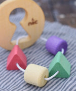 Close up of the coloured shape pieces on the Nic Toys wooden threaded shape sorter. Wooden disk with a keyhole shape cut out in the middle with a piece of thread feeding through different coloured blocks in different coloured shapes.