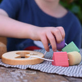 Child playing with the Nic Toys wooden threaded shape sorter. Wooden disk with a keyhole shape cut out in the middle with a piece of thread feeding through different coloured blocks in different coloured shapes.