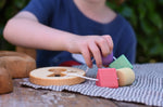Child playing with the Nic Toys wooden threaded shape sorter. Wooden disk with a keyhole shape cut out in the middle with a piece of thread feeding through different coloured blocks in different coloured shapes.