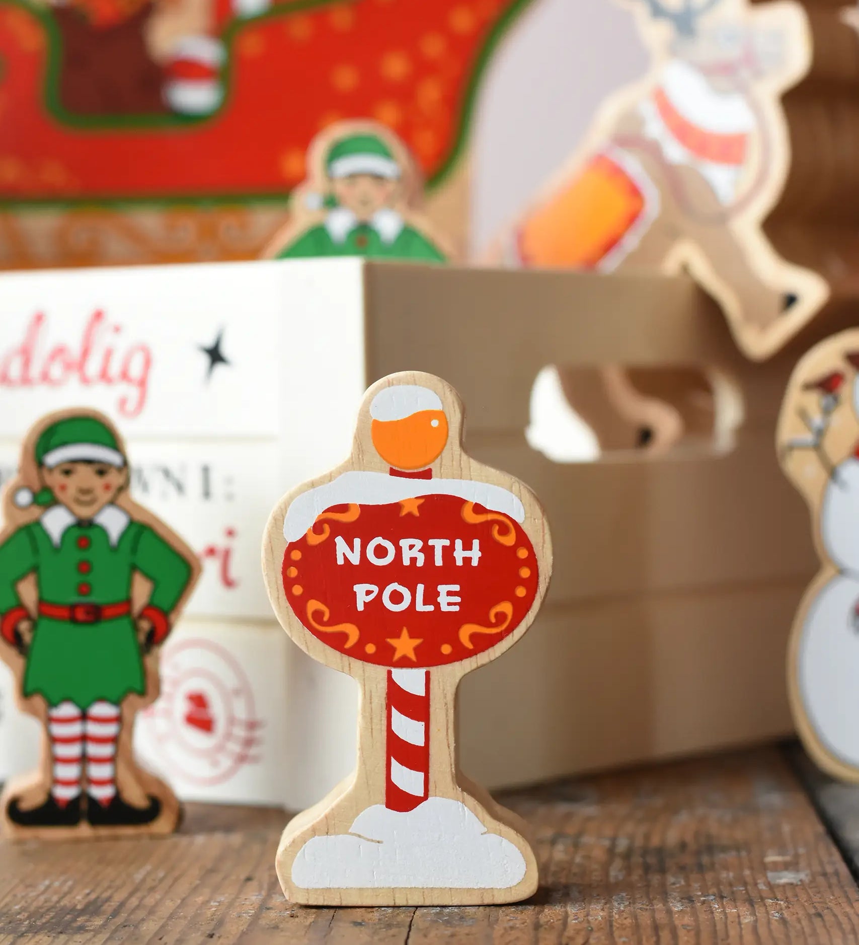 Lanka Kade red north pole sign wooden toy figure placed on a wooden surface in the Babipur playroom with other festive figures in teh background.